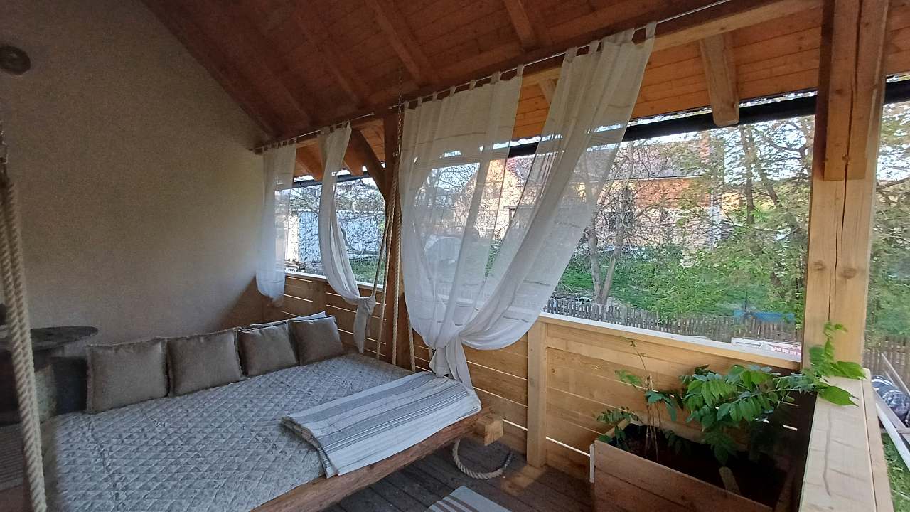 Krytá veranda se závěsnou postelí na lanech za lněnými závěsy